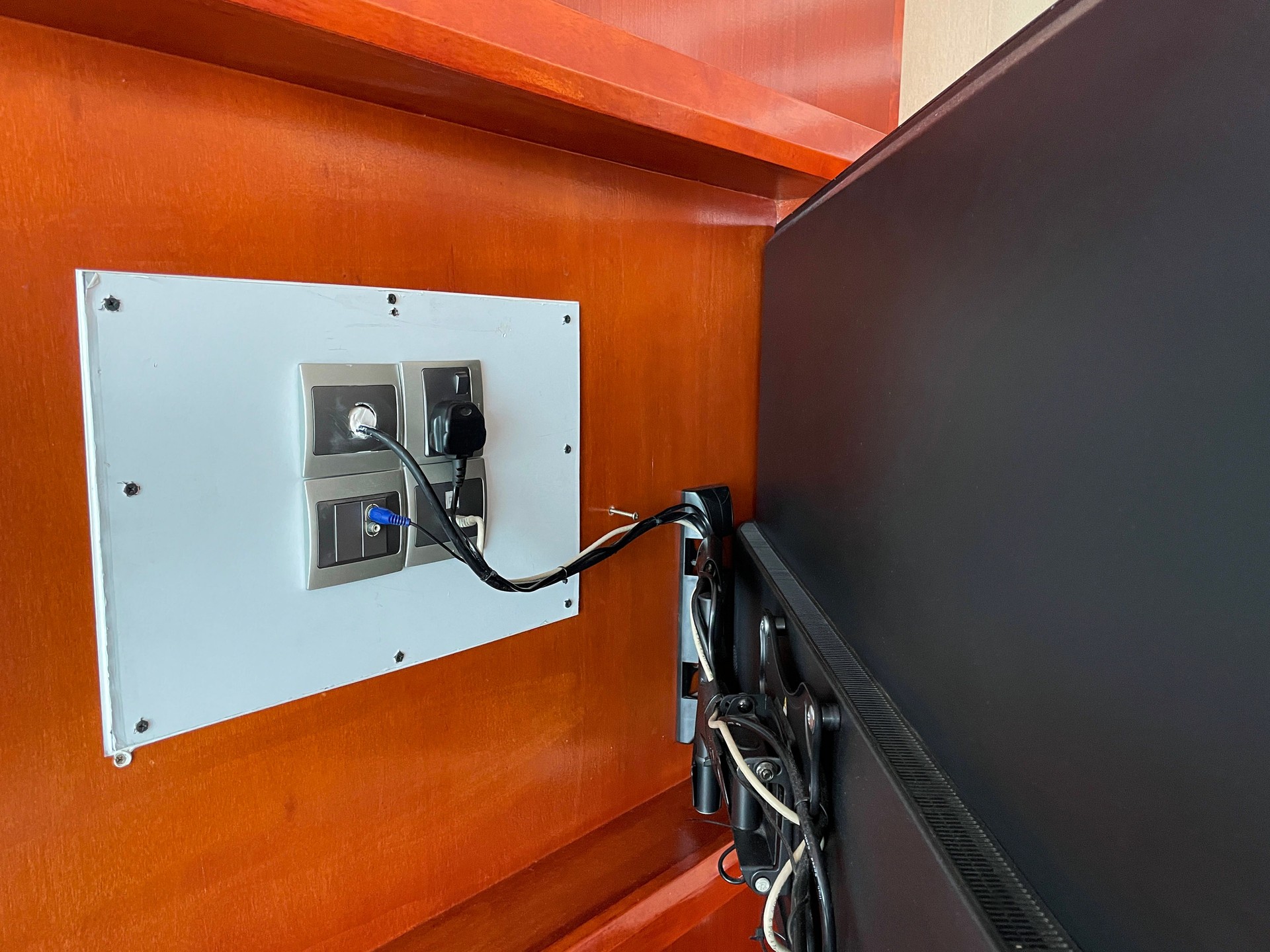 Close-up image of back of wall mounted television on bracket attached to wood panel wall, tidy hidden cables attached to aerial socket, wall plug socket, electric plug, focus on foreground